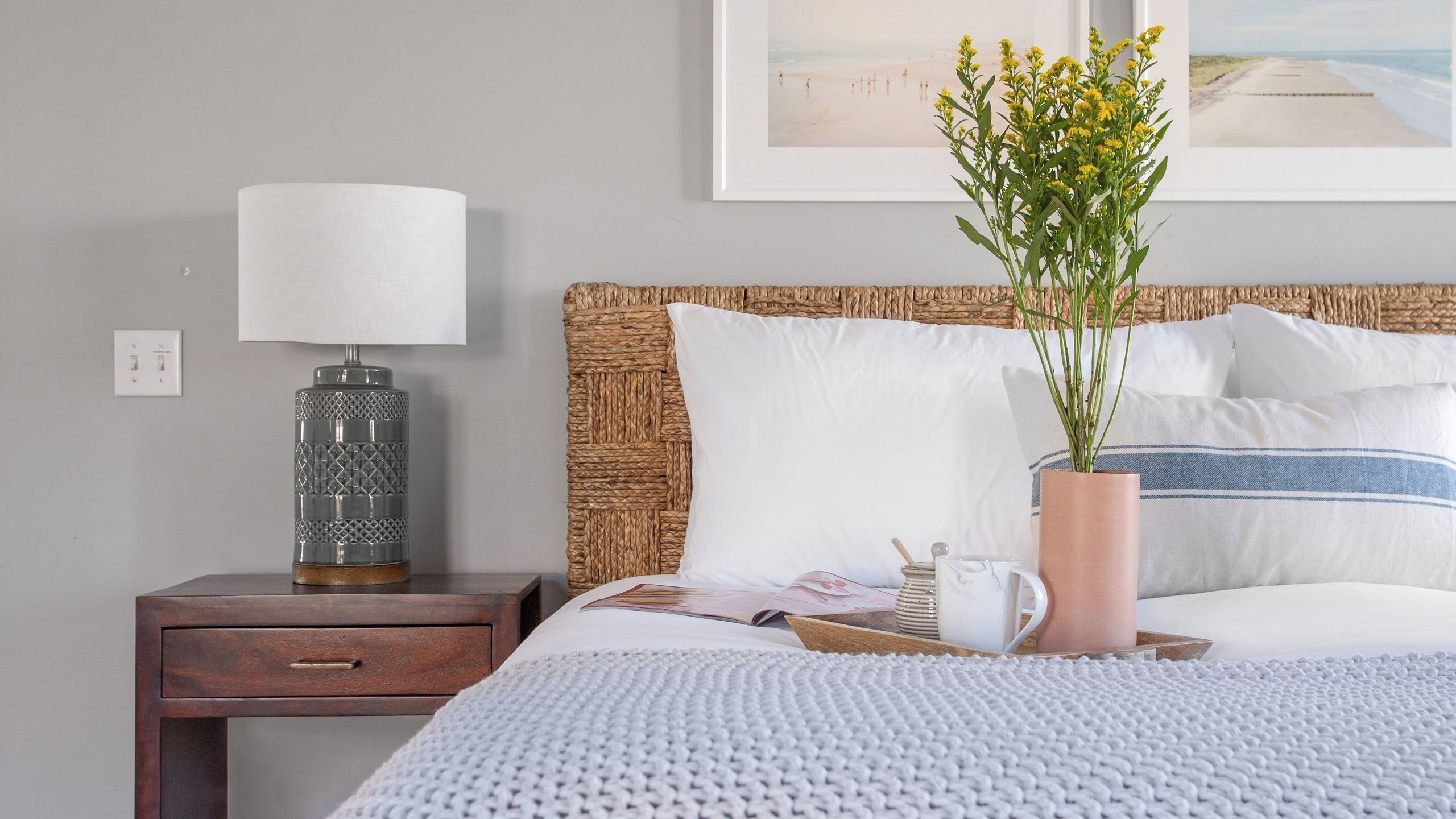 A neatly arranged hotel room with a bed, a bedside table with a lamp, a potted plant, and a framed picture on the wall.