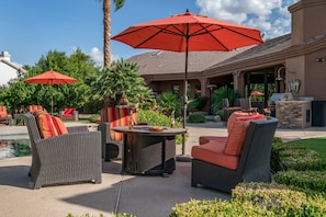 An outdoor patio area with wicker furniture, red umbrellas, and a grill.