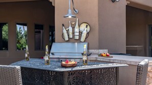 An outdoor bar area with a grill, decorative wall art, and seating. - Preston by Avantstay 6BR Desert Oasis w/ Basketball Court, Pool & Hot Tub (Scottsdale)