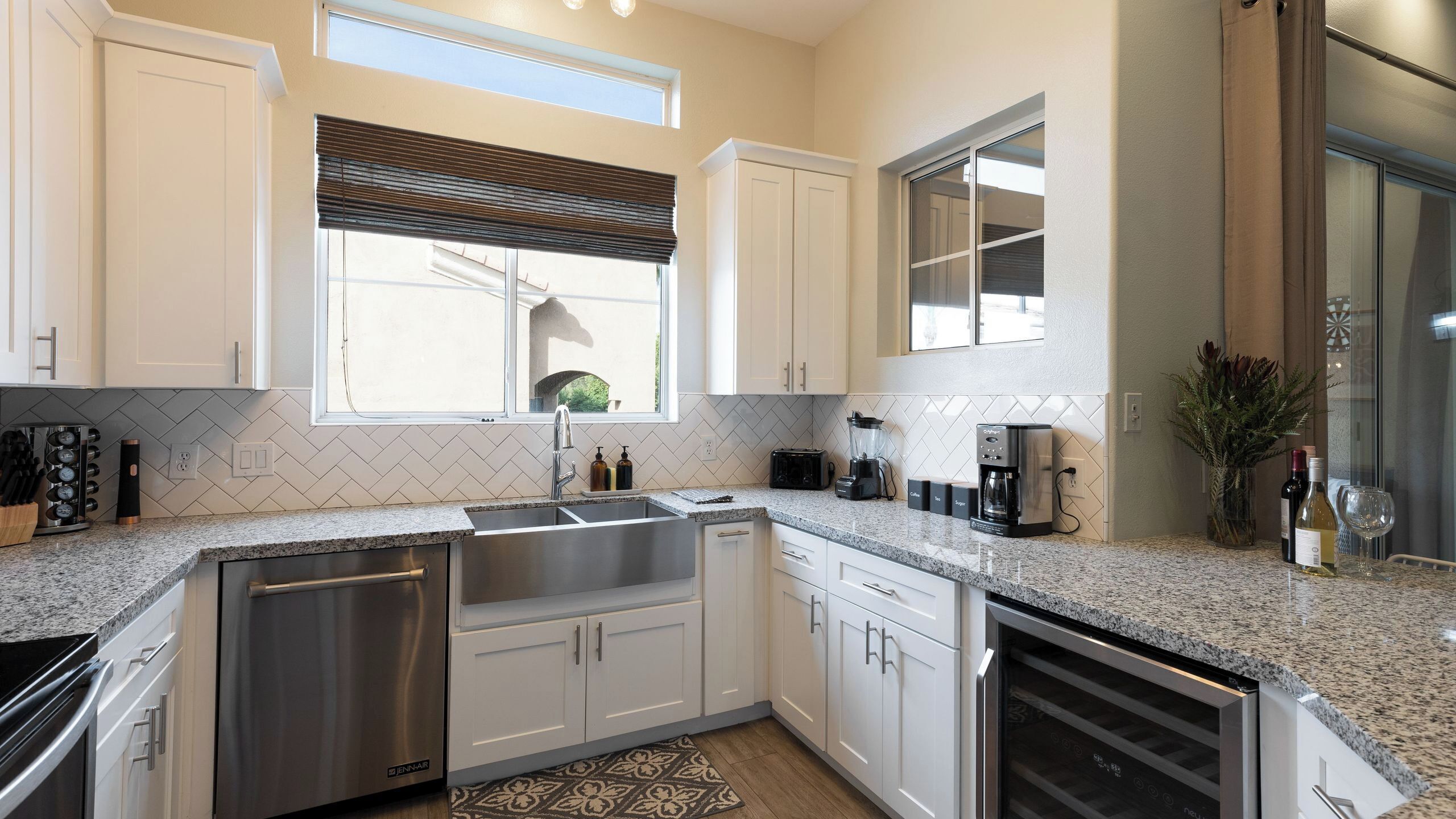 A modern kitchen with white cabinetry, a stainless steel dishwasher, a built-in oven, and a coffee maker.