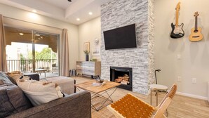 A modern living room with a fireplace, a flat-screen TV, and two guitars on the wall. - Eucalyptus by Avantstay Stunning Scottsdale Home w/ Communal Pool & Hot Tub (Scottsdale)