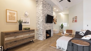 A living room with a stone fireplace, a flat-screen TV, a sofa, a coffee table, and a wooden cabinet.