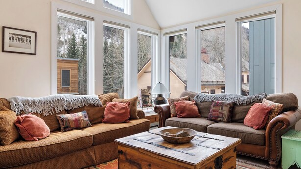 A cozy living room with two sofas, a coffee table, and large windows offering a view of a house and trees. - Legacy House by Avantstay Beautiful 4bdr Home in Great Location w/ Hot Tub (Telluride)