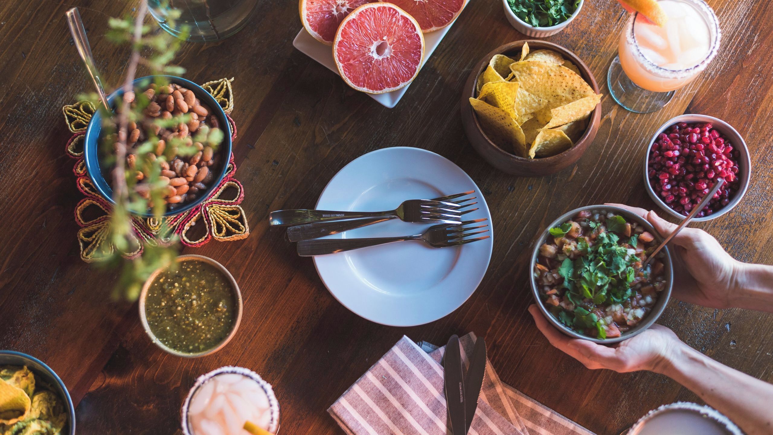 A table with various dishes, including chips, a salad, and a drink, suggesting a dining setting.