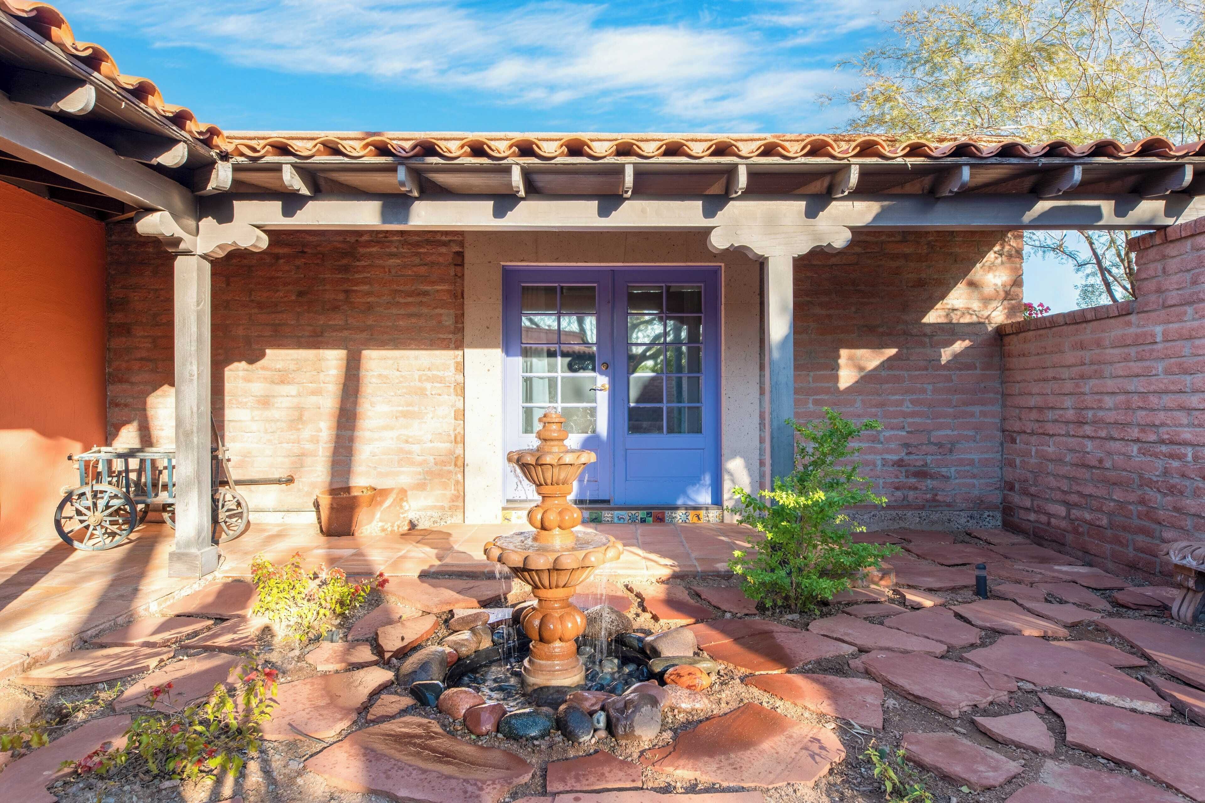 A courtyard with a stone fountain, a blue door, and a wheelbarrow.