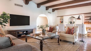 A living room with a television, sofa, armchair, coffee table, and a plant.