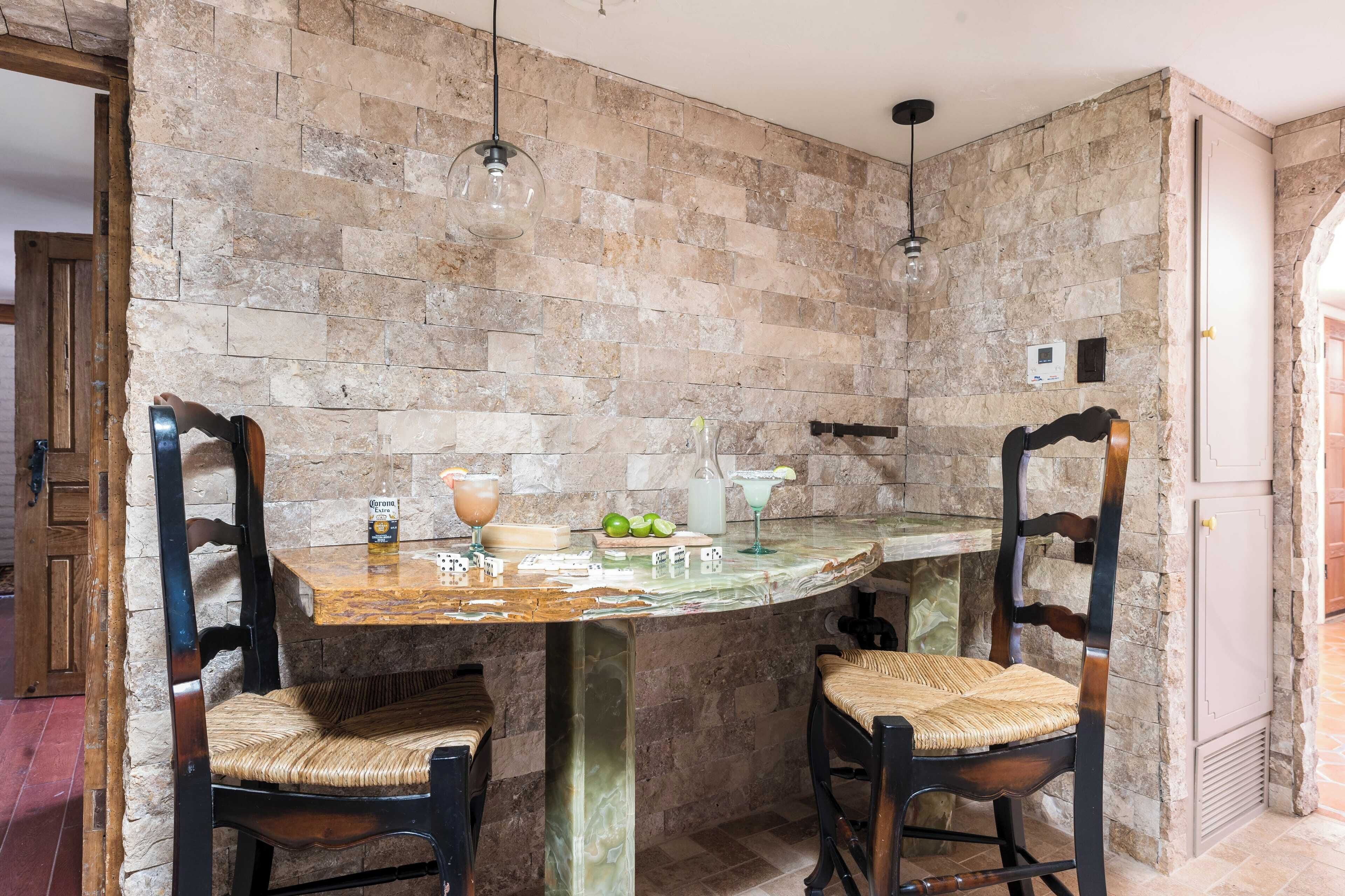 Eine Bar mit Steinwänden, zwei Holzsesseln, einem Marmortisch und hängenden Pendelleuchten.