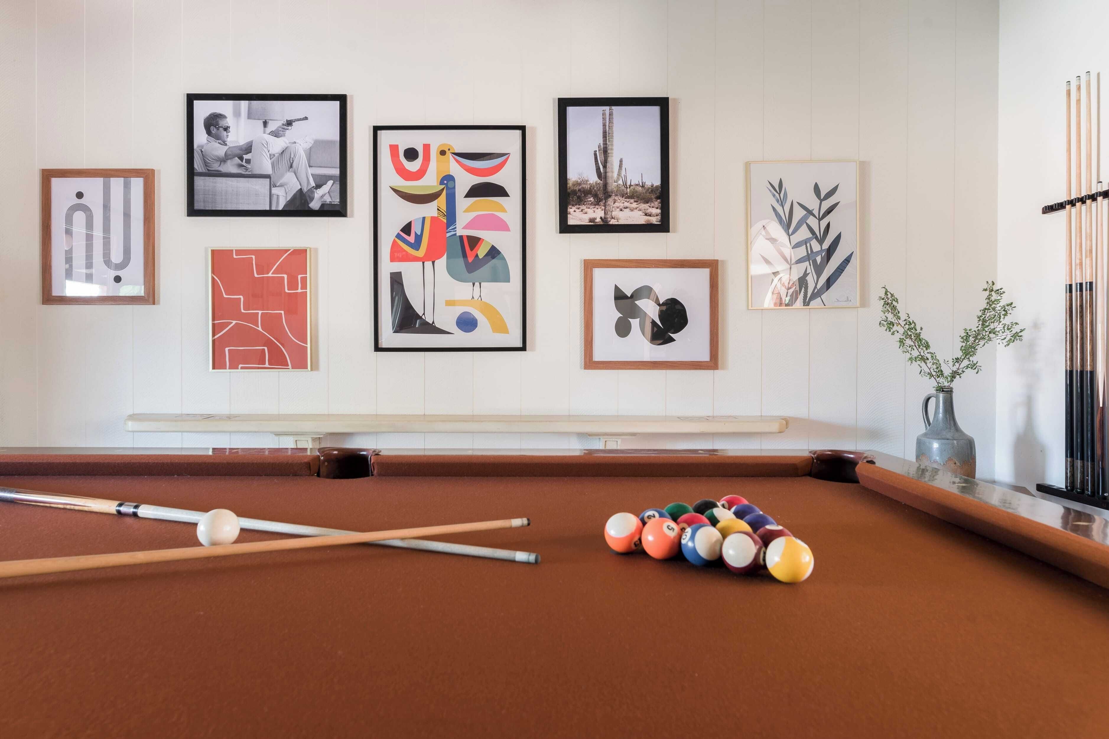 A pool table with balls and cues, surrounded by framed artworks on the wall.