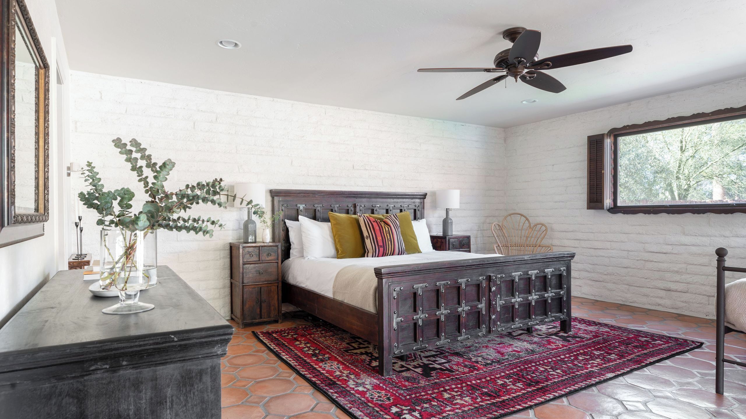 A bedroom with a bed, a nightstand, a dresser, a ceiling fan, and a window.