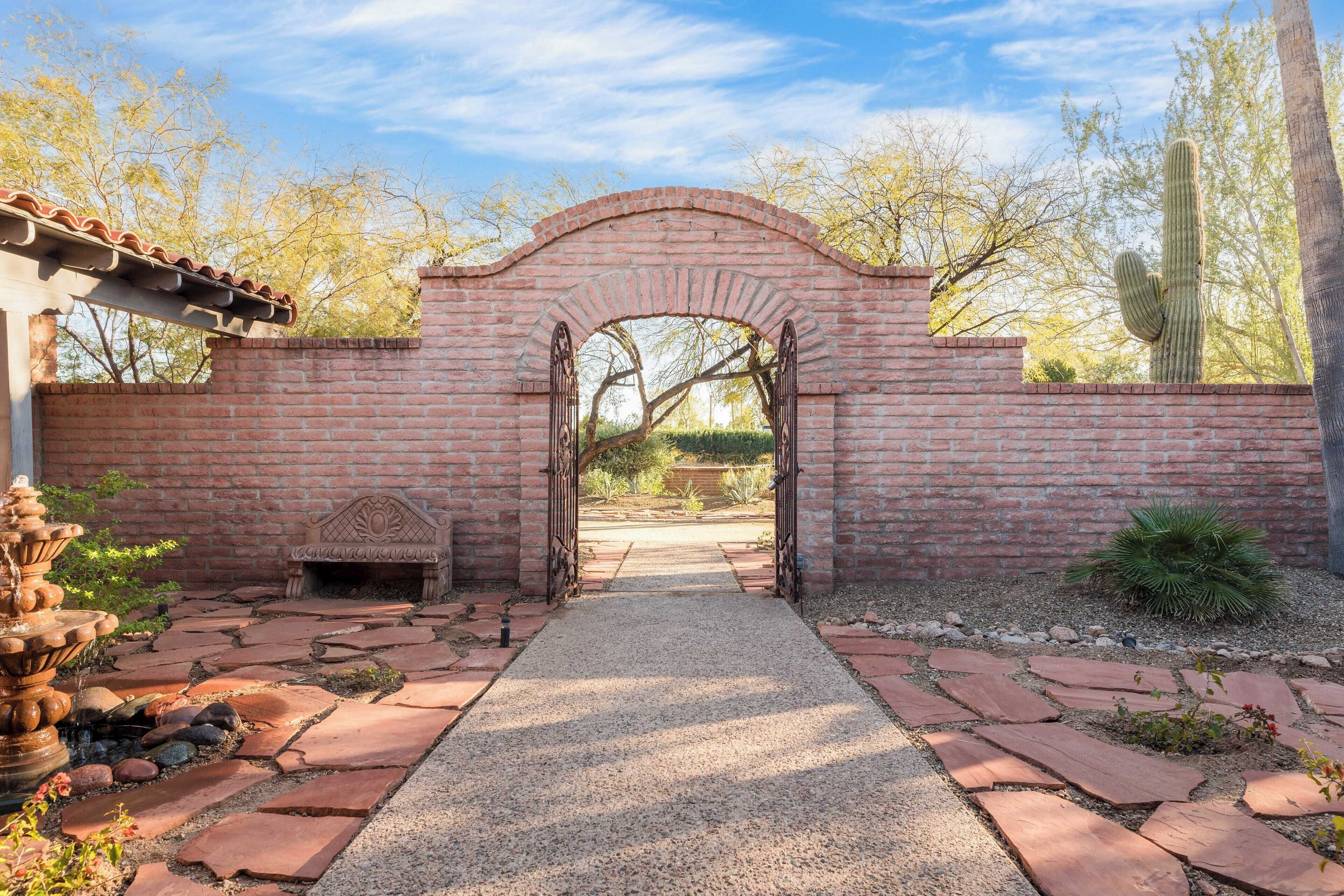 Un arc en briques mène à un jardin agrémenté d’un sentier en pierre, d’une fontaine et d’un cactus.