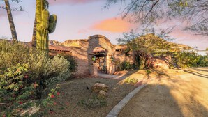 A historic building with an arched entrance, surrounded by cacti and desert vegetation.