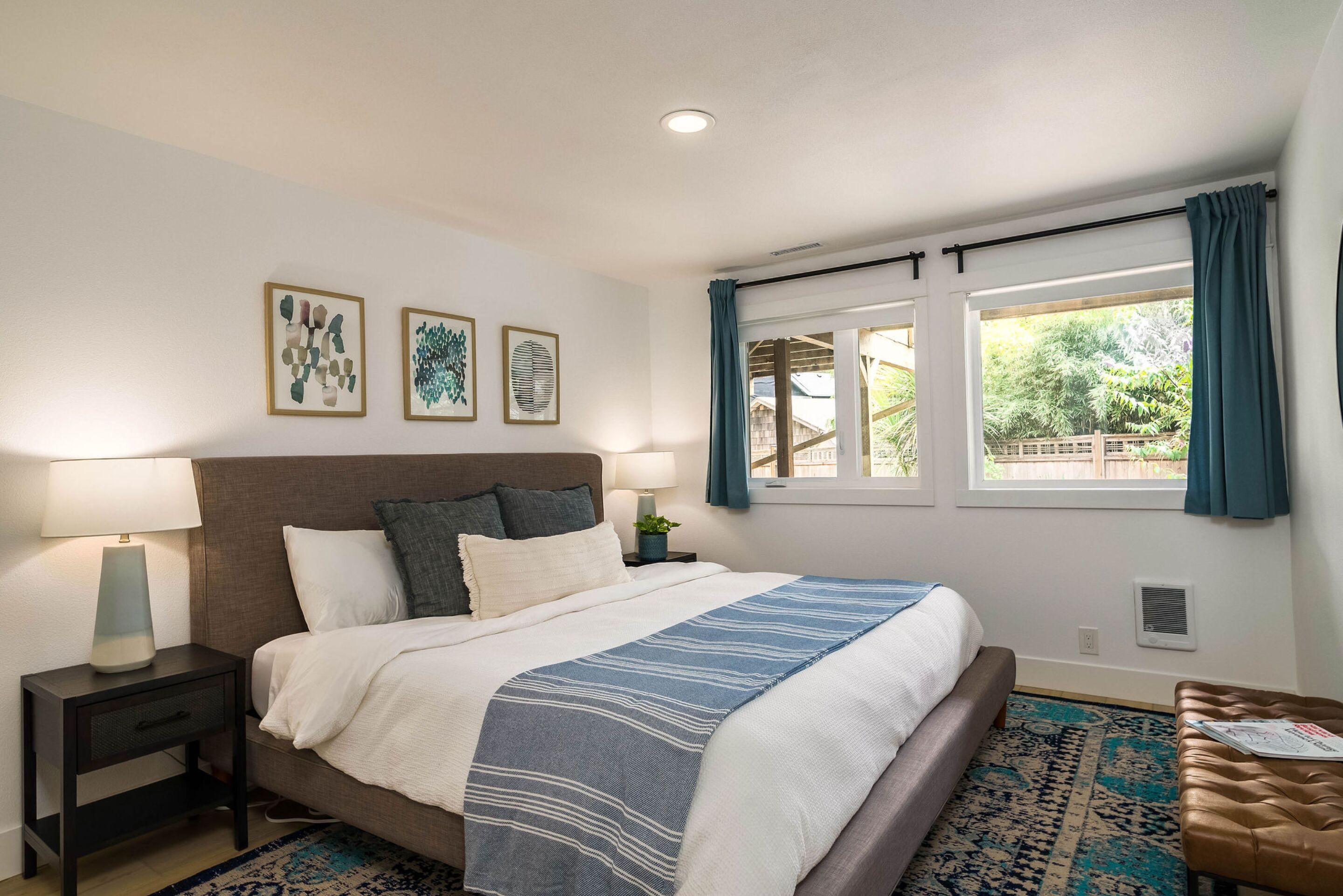 A bedroom with a bed, bedside tables, a window with curtains, and artwork on the wall.