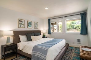 A bedroom with a bed, bedside tables, a window with curtains, and artwork on the wall.