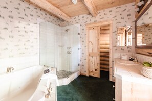 A bathroom with a glass-enclosed shower, a white bathtub, and wooden cabinetry. - Grizzly by Avantstay Rustic Big Bear Cabin w/ Hot Tub & Pool Table (Big Bear Lake)