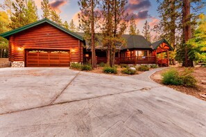 A log cabin with a garage and a covered porch, surrounded by trees and a concrete driveway. - Grizzly by Avantstay Rustic Big Bear Cabin w/ Hot Tub & Pool Table (Big Bear Lake)
