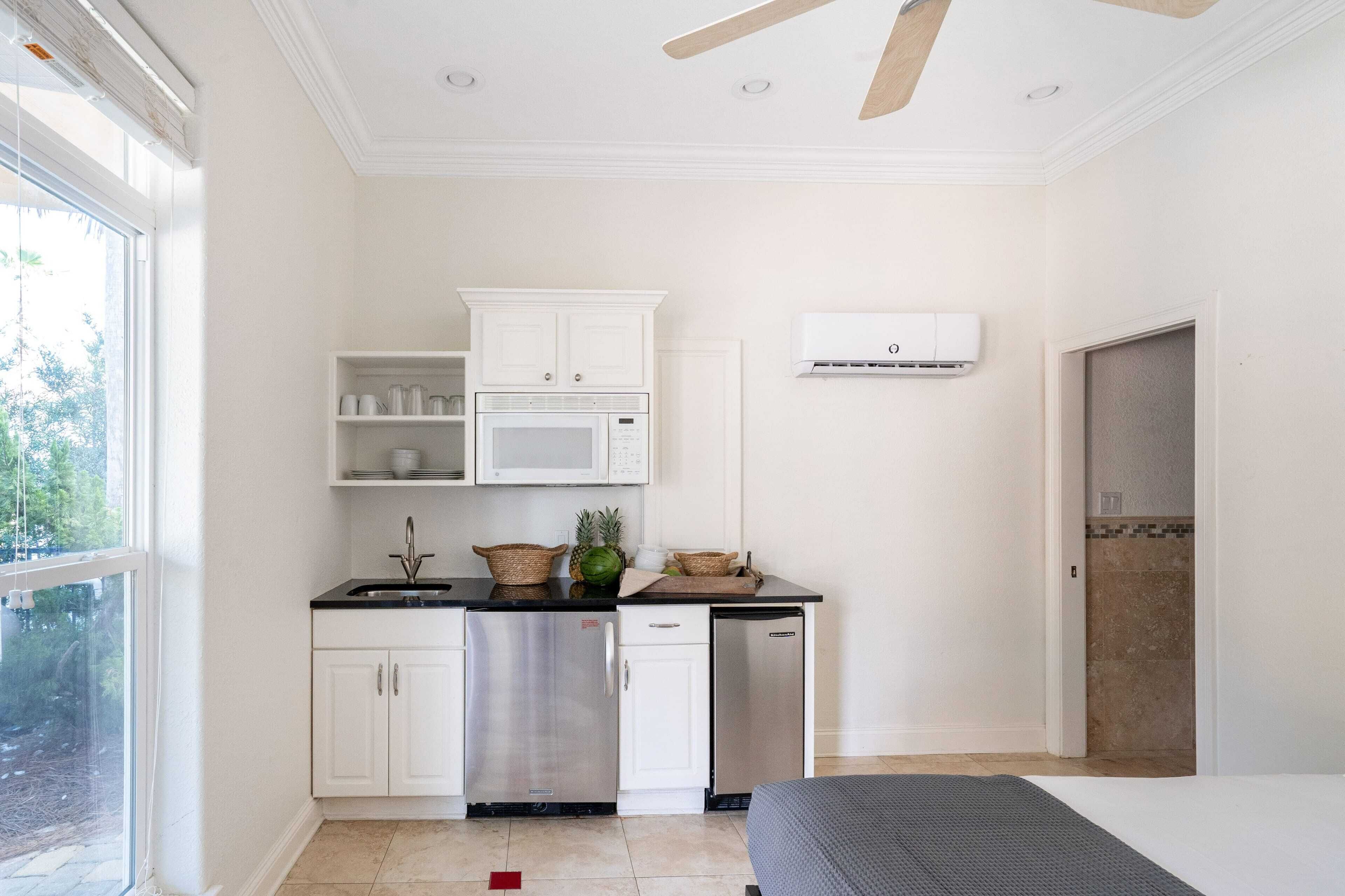 Cocina pequeña con armarios blancos, microondas y lavavajillas. Hay una ventana que proporciona luz natural y vistas al exterior con vegetación.