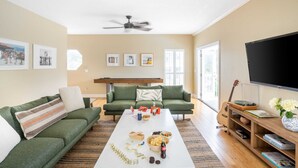 Una sala de estar con un sofá verde, una mesa de centro con aperitivos y bebidas, un televisor de pantalla plana y una guitarra.