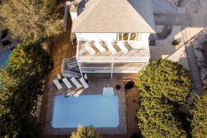An aerial view of a house with a swimming pool, a covered outdoor area with seating, and a staircase leading to a balcony.