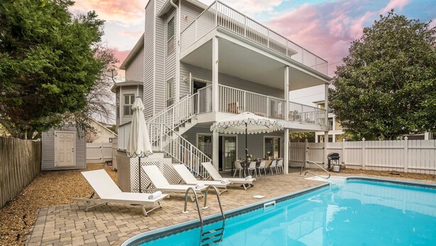 Una casa de dos pisos con piscina, muebles de exterior y un patio cubierto.