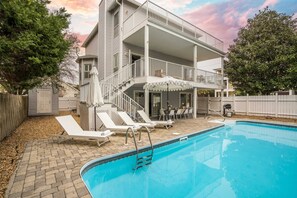 Ein zweigeschossiges Haus mit Swimmingpool, Gartenmöbeln und einer überdachten Terrasse.