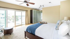 Un dormitorio con cama, ventilador de techo, ventana grande y puerta corrediza a un balcón.