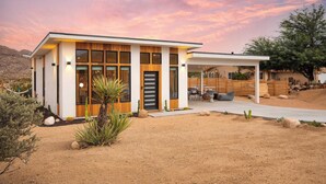 A modern house with a large garage, a patio, and a desert landscape. - Chicory by Avantstay Modern Desert Retreat w/ Hot Tub (Joshua Tree)
