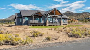 A two-story house with a large deck, surrounded by a dry, rocky landscape with sparse vegetation. - Pioneer by Avantstay Magnificent Home Located In The Brasada Ranch Community! (Powell Butte)