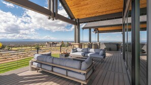 A covered outdoor deck with a sofa and a hot tub. - Pioneer by Avantstay Magnificent Home Located In The Brasada Ranch Community! (Powell Butte)