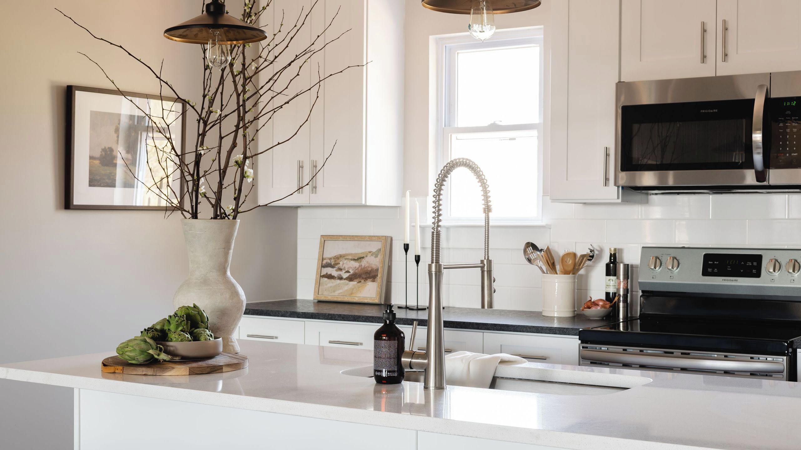A modern kitchen with white cabinetry, a large island, a stainless steel refrigerator, and a microwave.