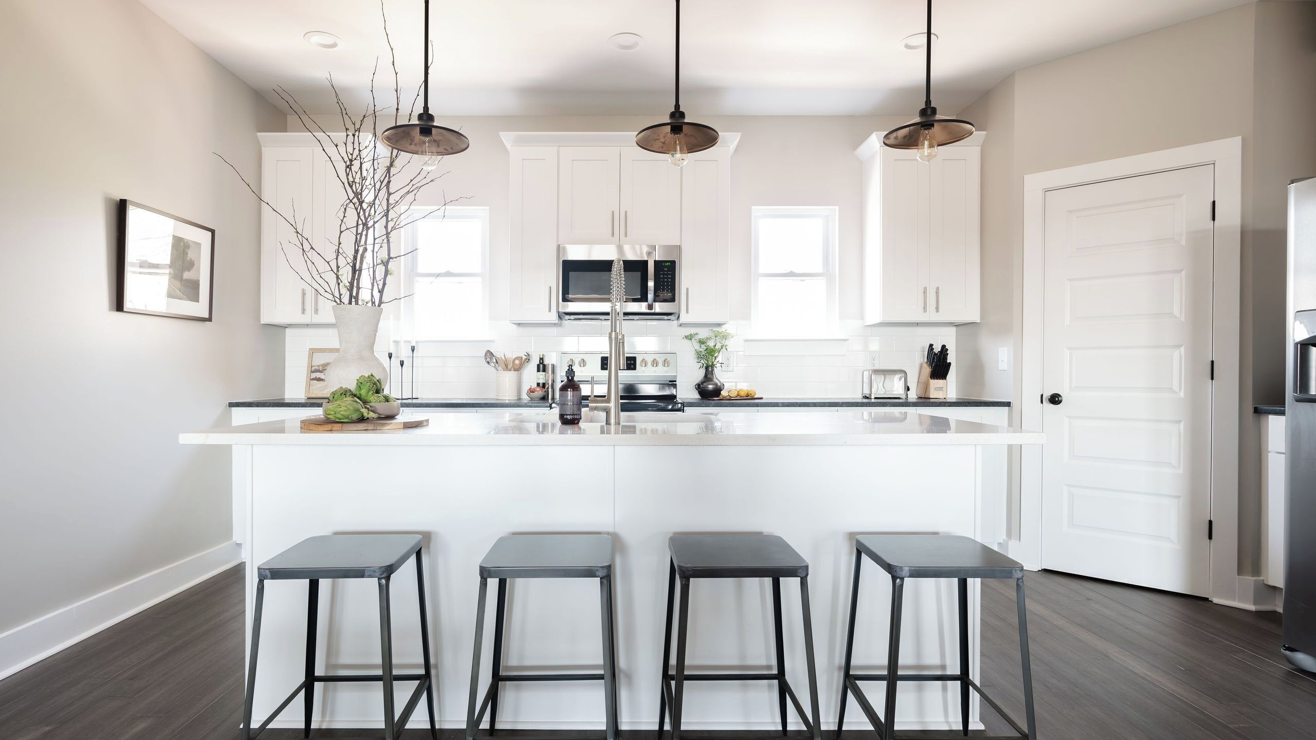 A modern kitchen with white cabinets, a central island, bar stools, and pendant lighting.