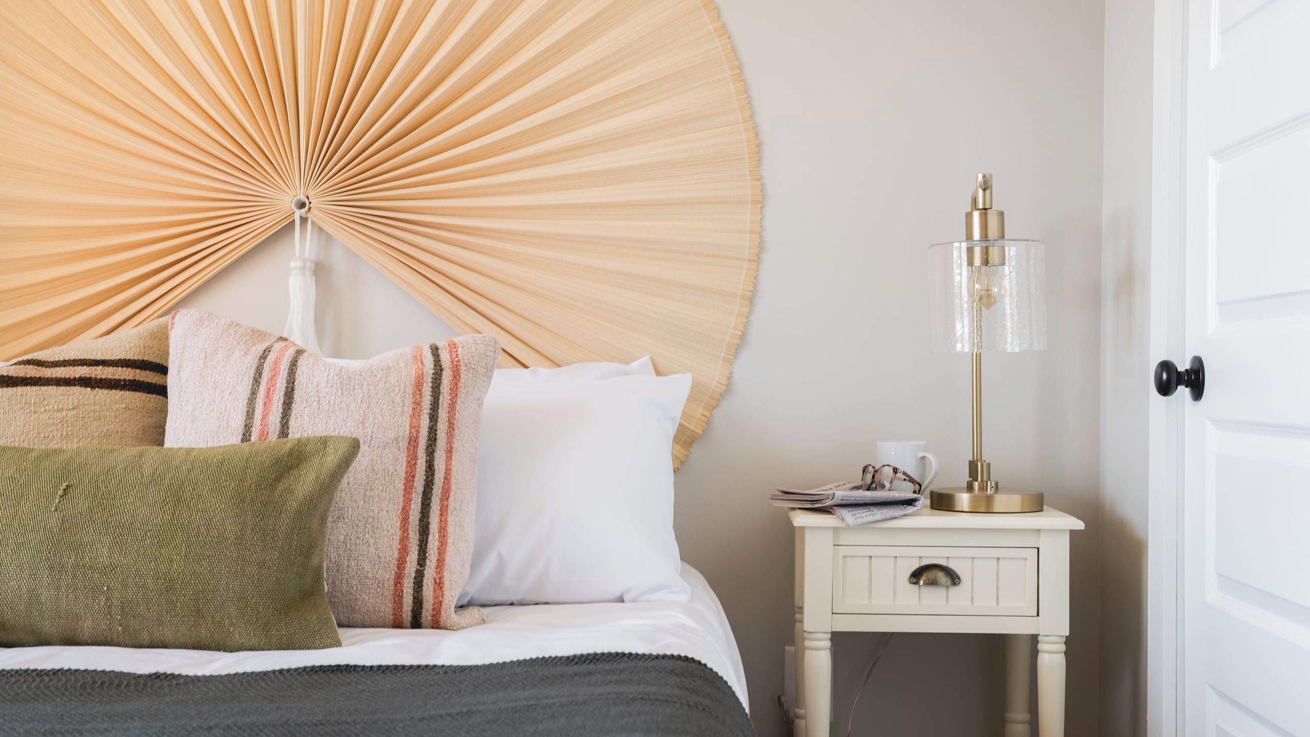 A neatly made bed with pillows, a bedside table with a lamp, and a door.