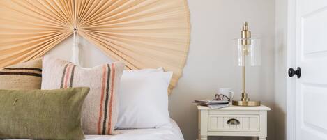 A neatly made bed with pillows, a bedside table with a lamp, and a door.