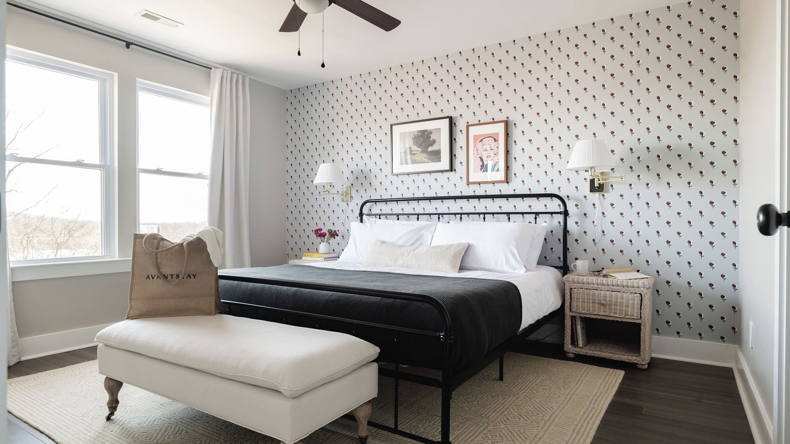 A bedroom with a bed, a nightstand, a lamp, a window, and a bag on the floor.
