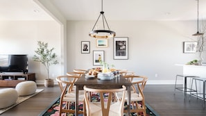 A dining area with a wooden table, six chairs, a chandelier, and a television in the background. - Rhett by Avantstay Stylish Southern Style Townhouse w/ Gorgeous Design (Nashville)