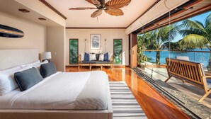 Ein modernes Hotelzimmer mit einem großen Bett, einem Deckenventilator, einem Balkon mit Blick auf Palmen und das Meer.