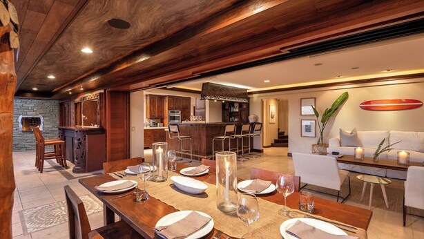 A spacious dining area with a long wooden table set for a meal, a bar area with wooden cabinets, and a living room with a sofa and decorative items.