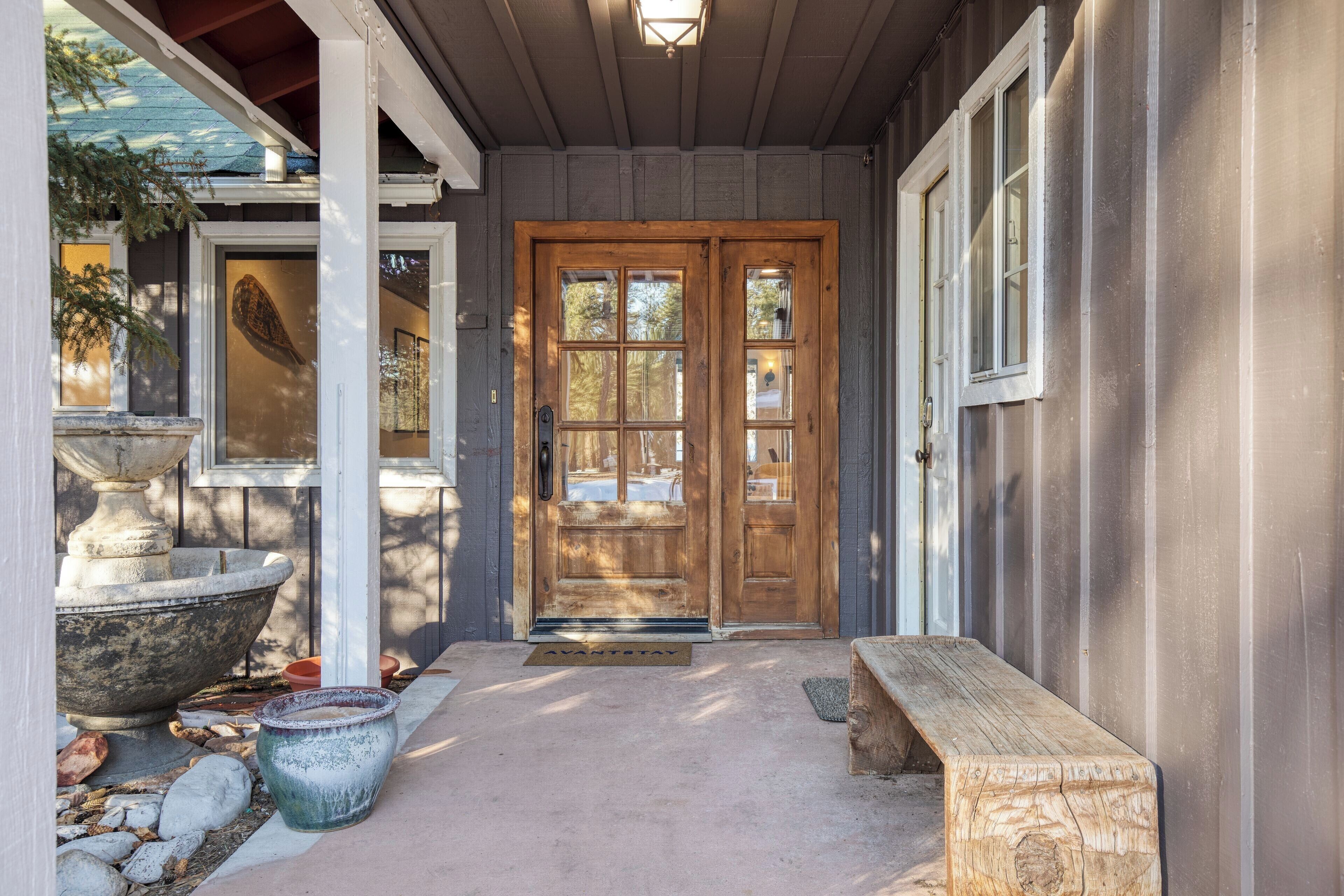 A wooden front door with a glass panel, a stone planter, and a wooden bench outside a building.