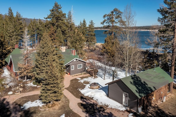 A cabin with a green roof, surrounded by trees and a lake view.