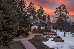 A cabin with a stone fireplace, surrounded by trees and a brick pathway.