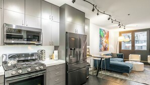 A modern kitchen with stainless steel appliances, a dining area with a sofa and table, and a large window. - New San Juan 303 by Avantstay Modern Penthouse w/ Deck Overlooking Main Street (Telluride)