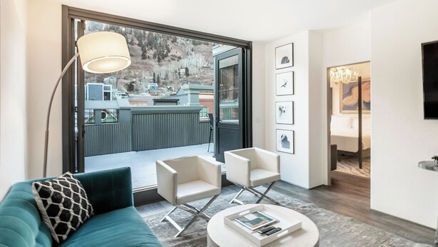 A modern living room with a teal sofa, two white armchairs, a round coffee table, a floor lamp, and a large window with a view of a mountain. - New San Juan 303 by Avantstay Modern Penthouse w/ Deck Overlooking Main Street (Telluride)
