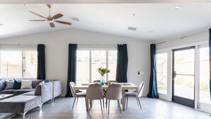 Ein modernes Wohnzimmer mit Essbereich, Deckenventilator, großen Fenstern mit Vorhängen und einem hellen Boden.