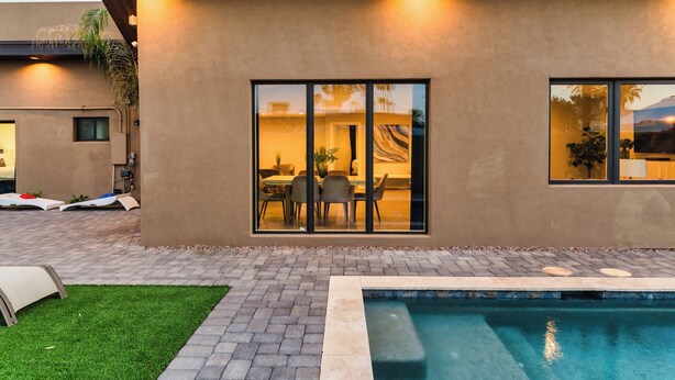 Ein modernes Haus mit Swimmingpool, einer Terrasse mit Liegestühlen und einem Essbereich, der durch große Fenster sichtbar ist.