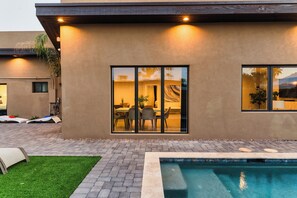 A modern house with a swimming pool, a patio with lounge chairs, and a dining area visible through large windows. - Sapphire By Avantstay Spacious Modern Getaway w/ Pool & Outdoor Grill (Scottsdale)