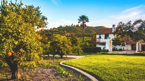 Ein Haus mit Garten, einem Weg und einer Hügelkulisse im Hintergrund.