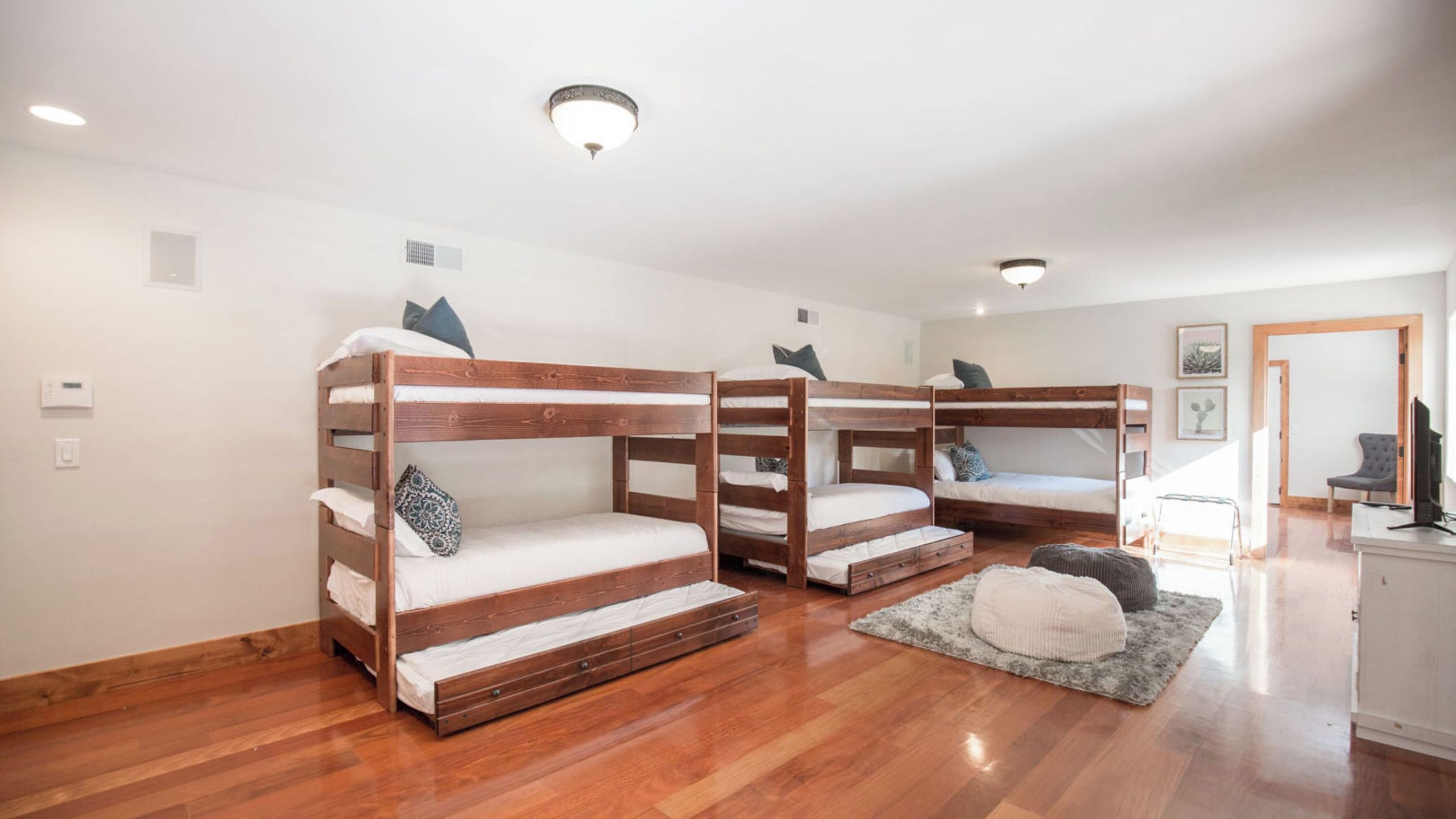 A room with four bunk beds, a wooden floor, a small rug, a chair, and a television.