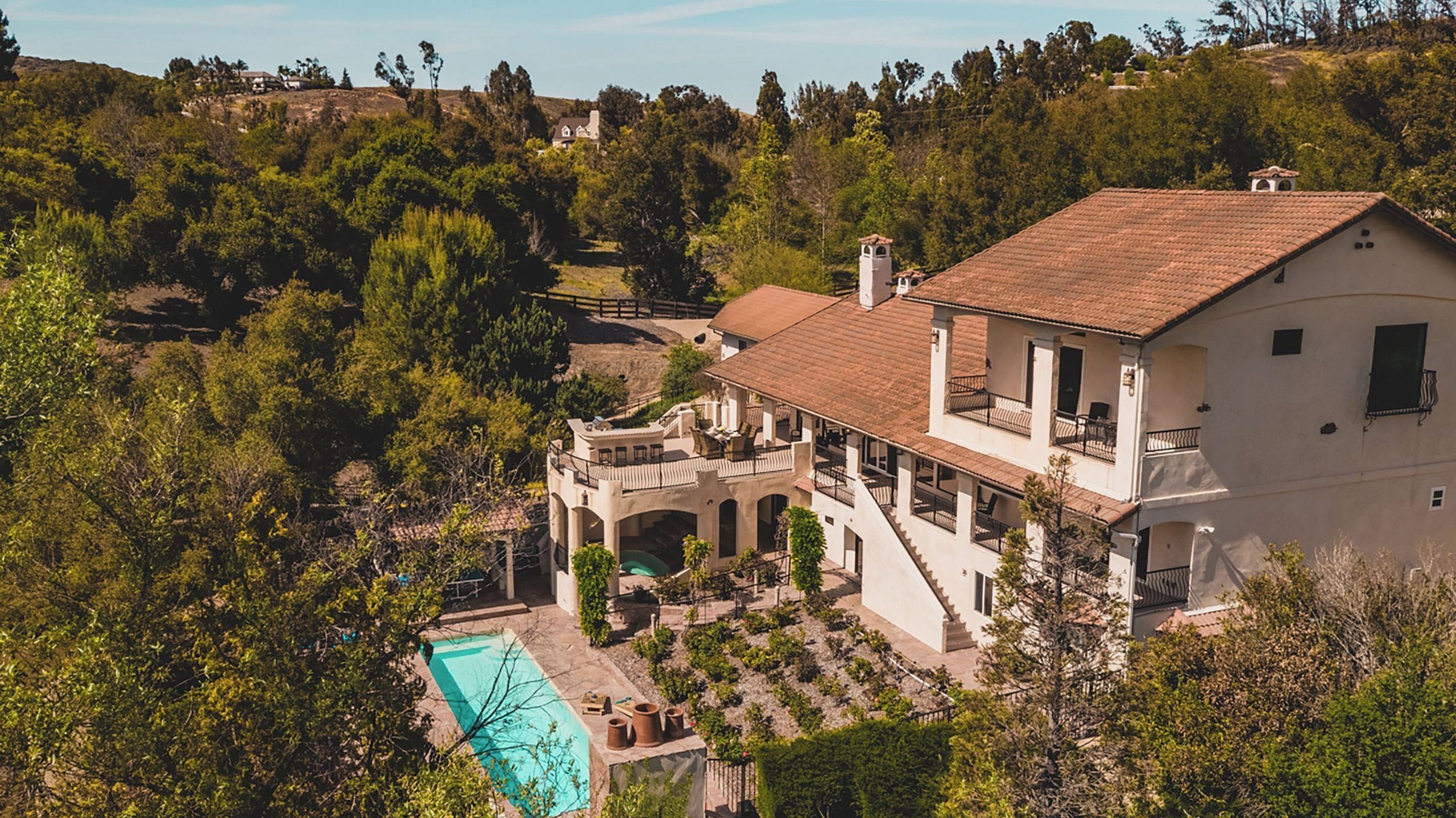A large house with a swimming pool, surrounded by trees and hills.