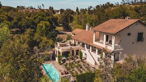 A large house with a swimming pool, surrounded by trees and hills.