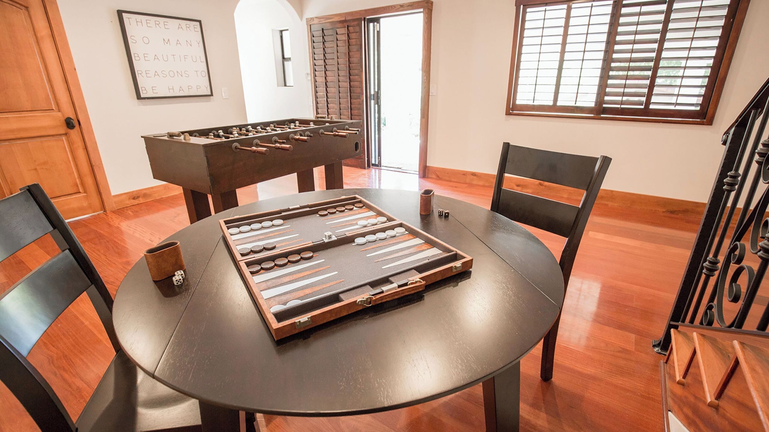 A dining table with a board game, chairs, a wooden door, a window, and a wall-mounted sign.