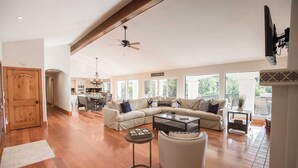 Ein geräumiges Wohnzimmer mit einer großen Eckcouch, einem Couchtisch und einem Kamin. Im Hintergrund ist ein Essbereich zu sehen, mit einer angrenzenden Küche.